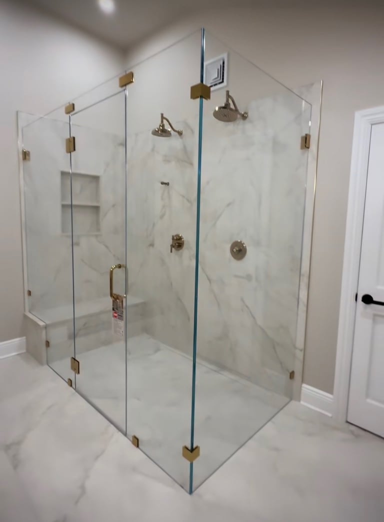 Modern glass shower enclosure with marble tile walls, brass hardware, and dual showerheads in a bathroom
