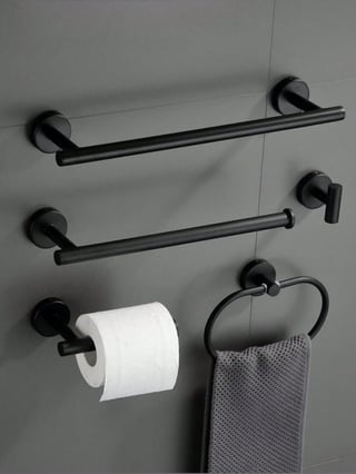 Black bathroom hardware mounted on gray wall including towel bars, toilet paper holder, and towel ring with a gray towel