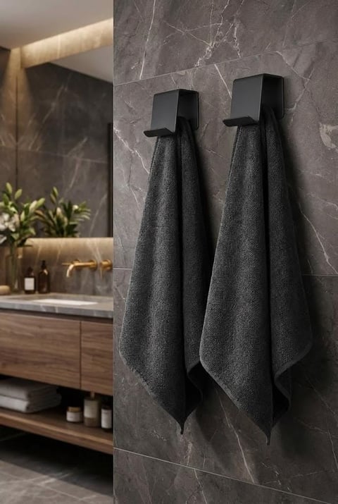 Two black towels hanging on sleek black hooks mounted on a dark gray marble bathroom wall