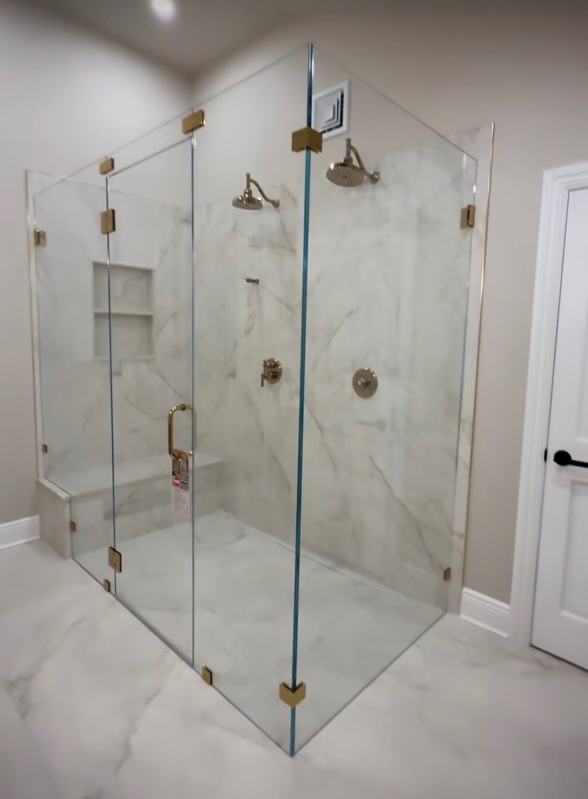 Modern frameless glass shower enclosure with brass hardware in a marble-tiled bathroom