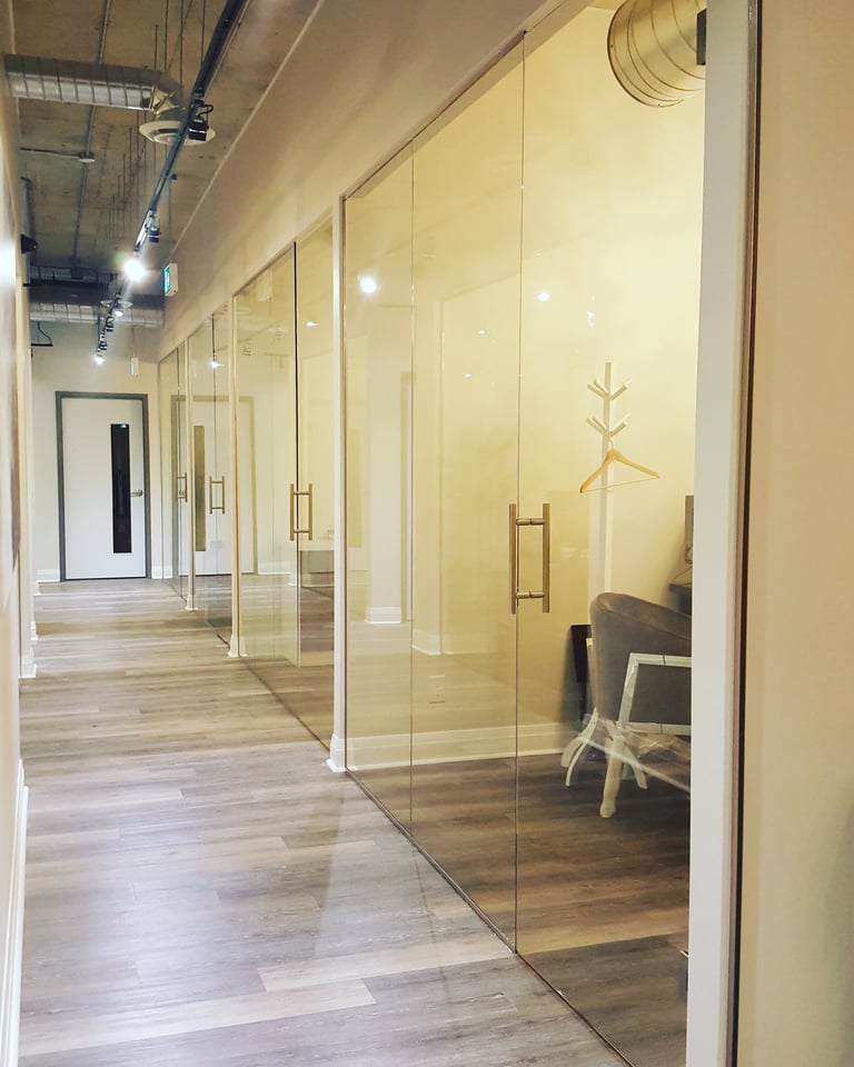 Modern office corridor with glass-walled conference rooms, wooden flooring, and minimalist furniture