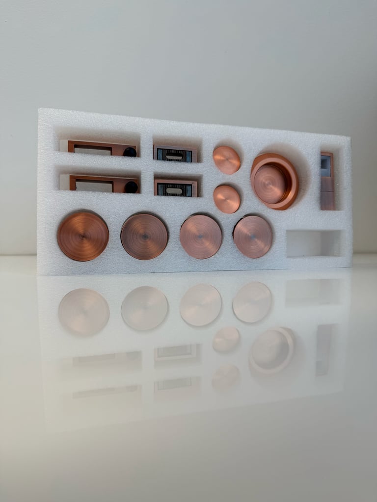 Copper-colored metal components organized in white foam packaging, including springs, discs, and cylindrical parts