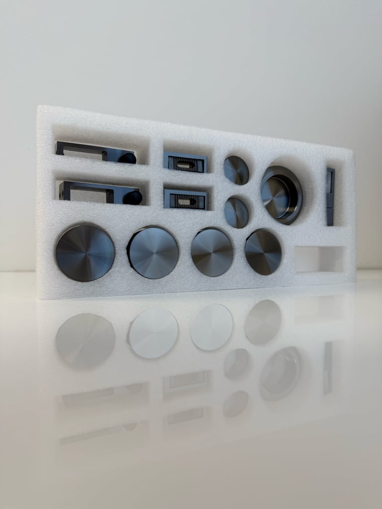 White foam tray containing various electronic components including metal knobs, switches, and circuit board elements arranged in compartments