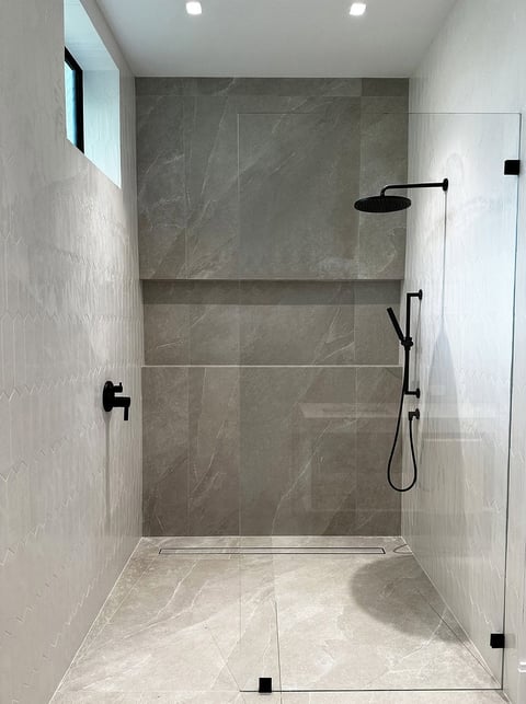 Modern shower enclosure with marble tile walls, glass door, overhead rain showerhead, and handheld spray with matte black fixtures
