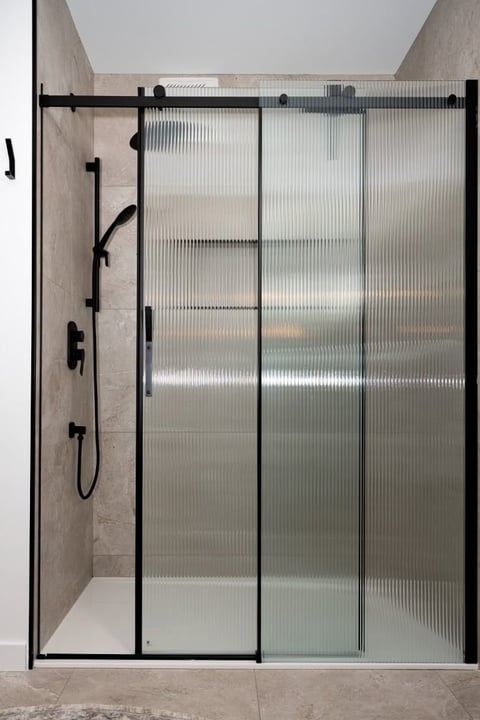 Modern frameless shower enclosure with black metal frame, fluted glass doors, and sliding mechanism in a tiled bathroom