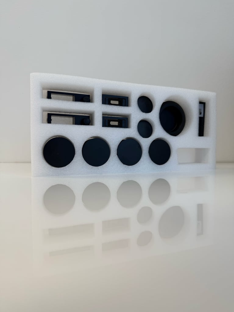 Foam storage organizer tray with compartments holding black and gray spheres, rectangular slots, and various sized circular objects